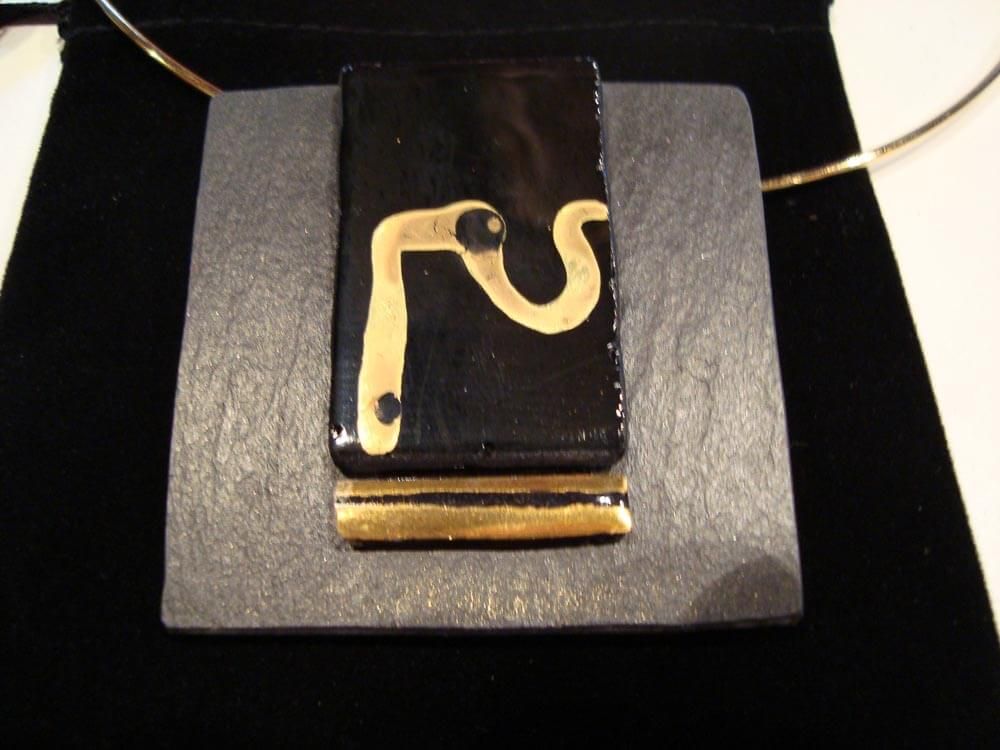 Collier pendentif noir et or sur une base carrée grise, sur fond de velours noir.