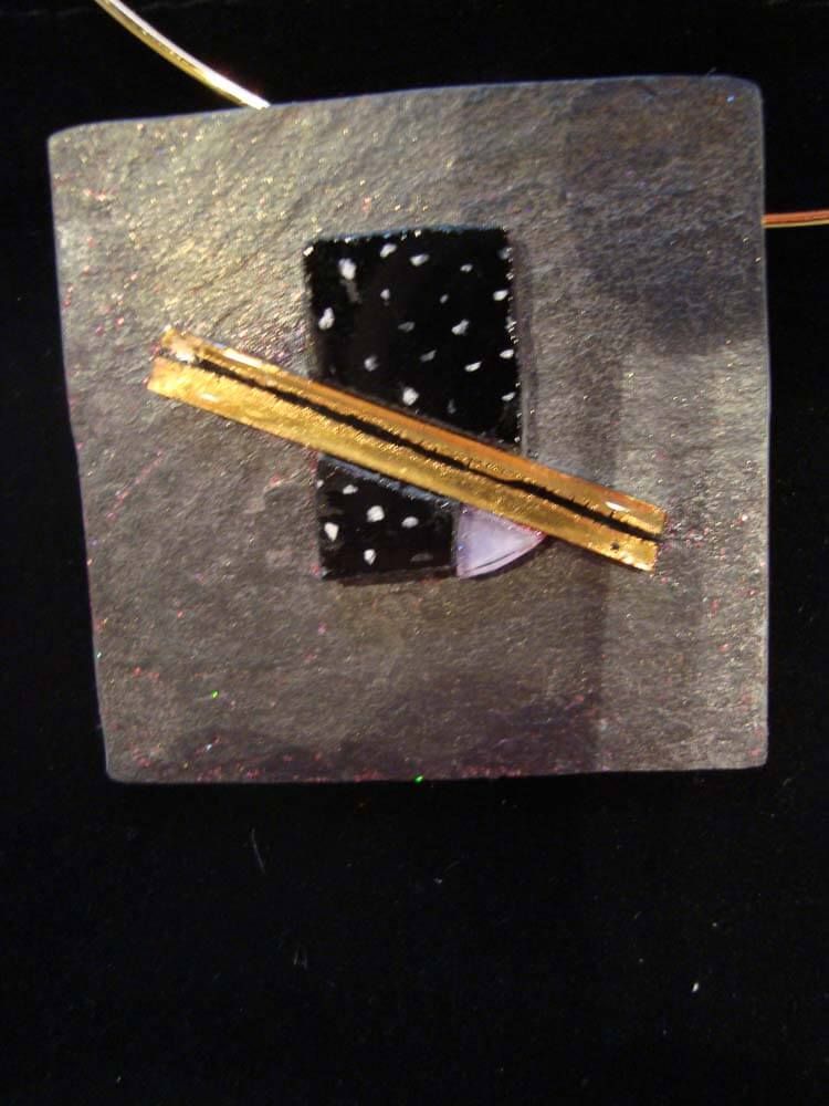 Pendentif géométrique or et noir sur une base carrée argentée ; rectangle noir à points blancs ; barre dorée.