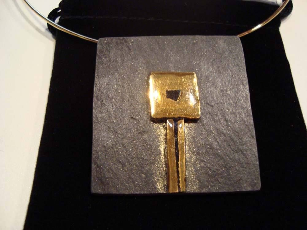 Collier pendentif argent et or sur velours noir : pierre grise carrée, carré doré, rayures dorées.