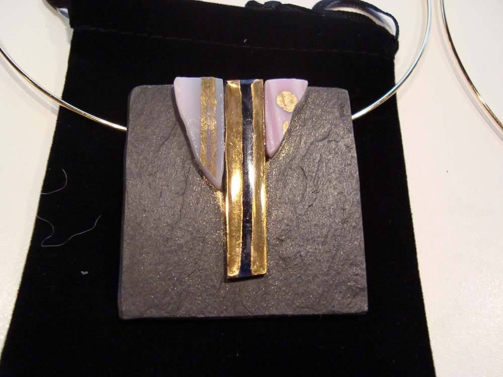 Collier pendentif carré en ardoise avec des accents dorés et lavande sur velours noir.