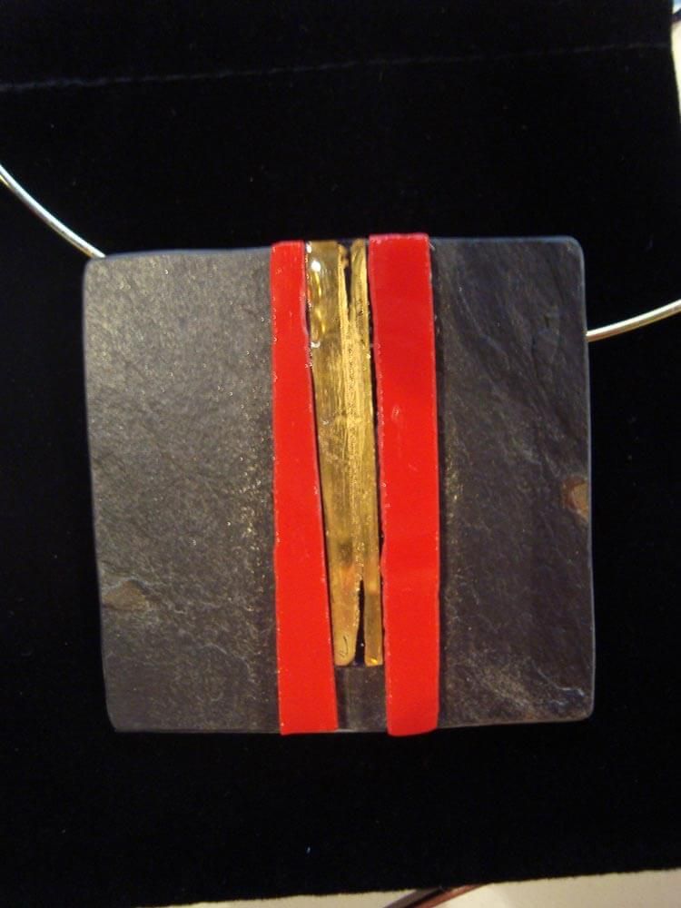 Collier pendentif carré avec pierre noire, bracelet rouge et détail doré.