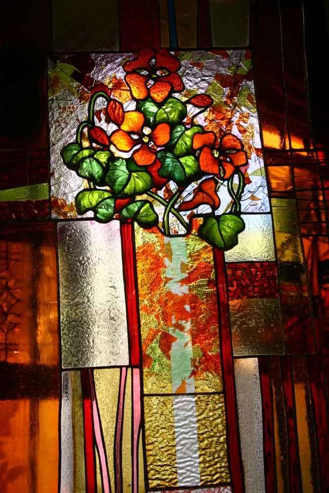 Vitrail à décor floral avec des fleurs rouge-orangé et des feuilles vertes sur une mosaïque de panneaux de verre colorés.