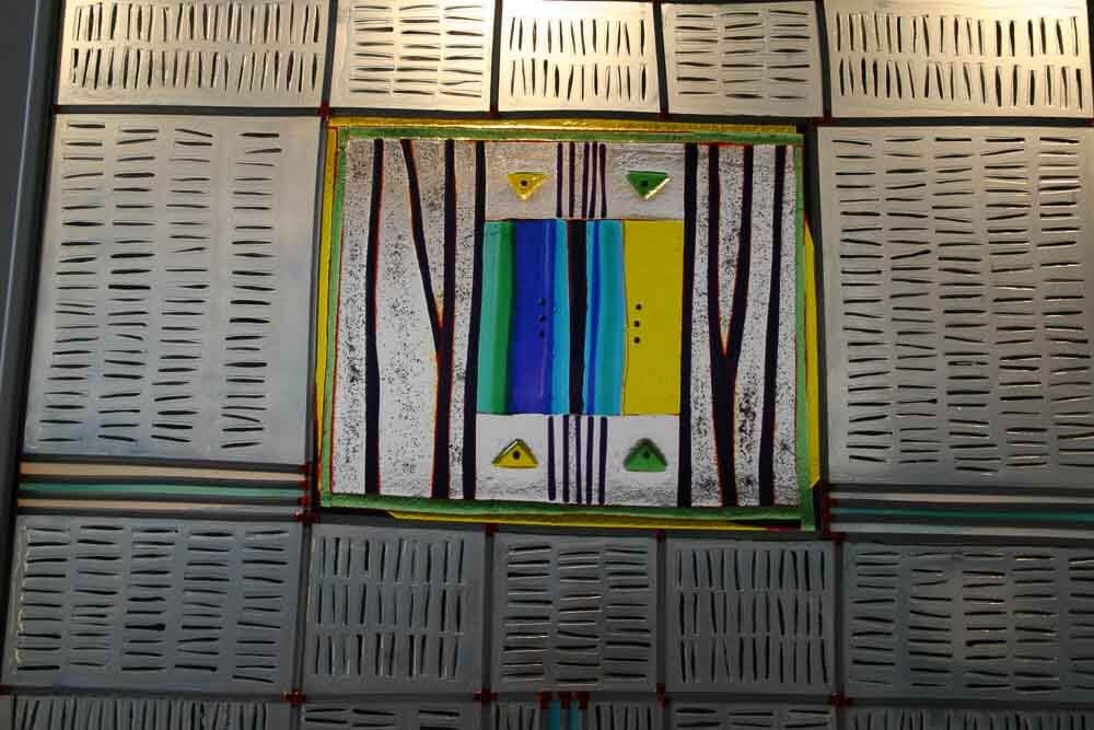 Œuvre abstraite : Pièce centrale rectangulaire à rayures verticales et à motifs arborés, entourée de panneaux métalliques aux lignes découpées.