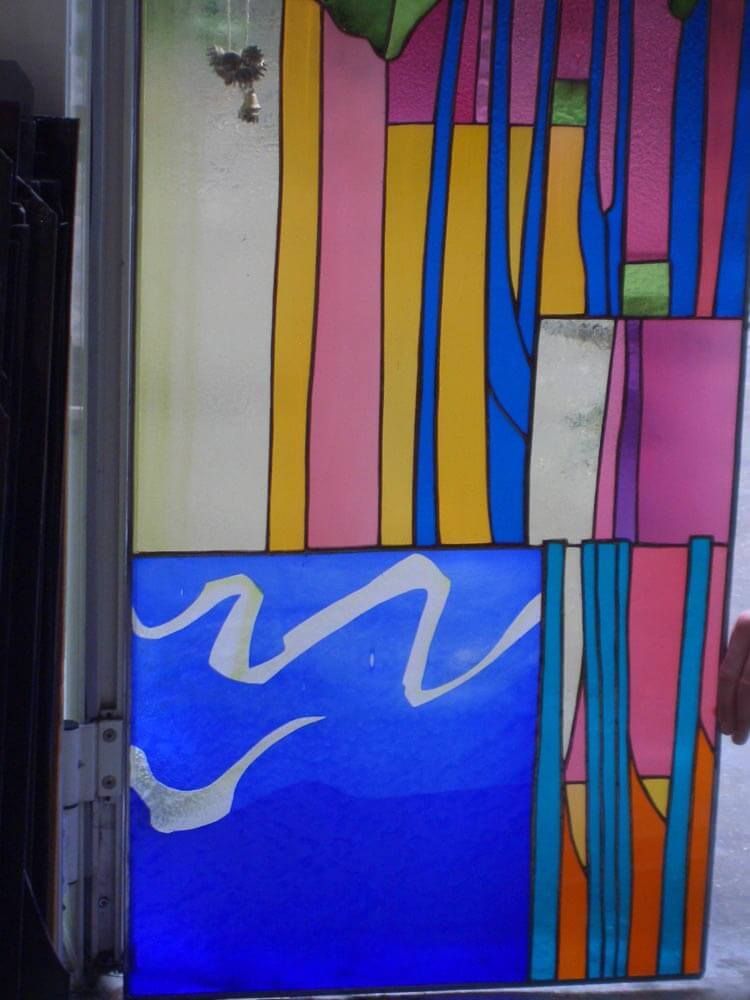 Vitrail orné de formes géométriques roses, jaunes, bleues et vertes ; un carré bleu avec des vagues blanches.