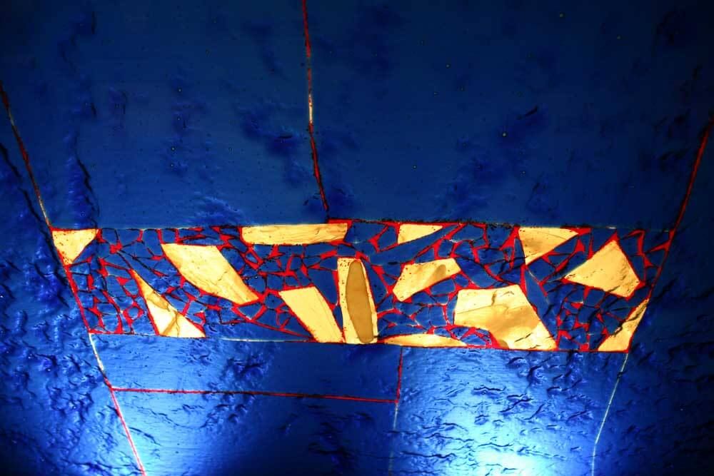 Œuvre abstraite aux formes dorées et bleues sur un mur bleu texturé.