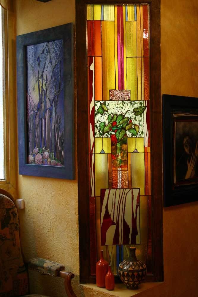 Vitrail à motif abstrait dans une niche ; un tableau à gauche ; des bouteilles sur le rebord.