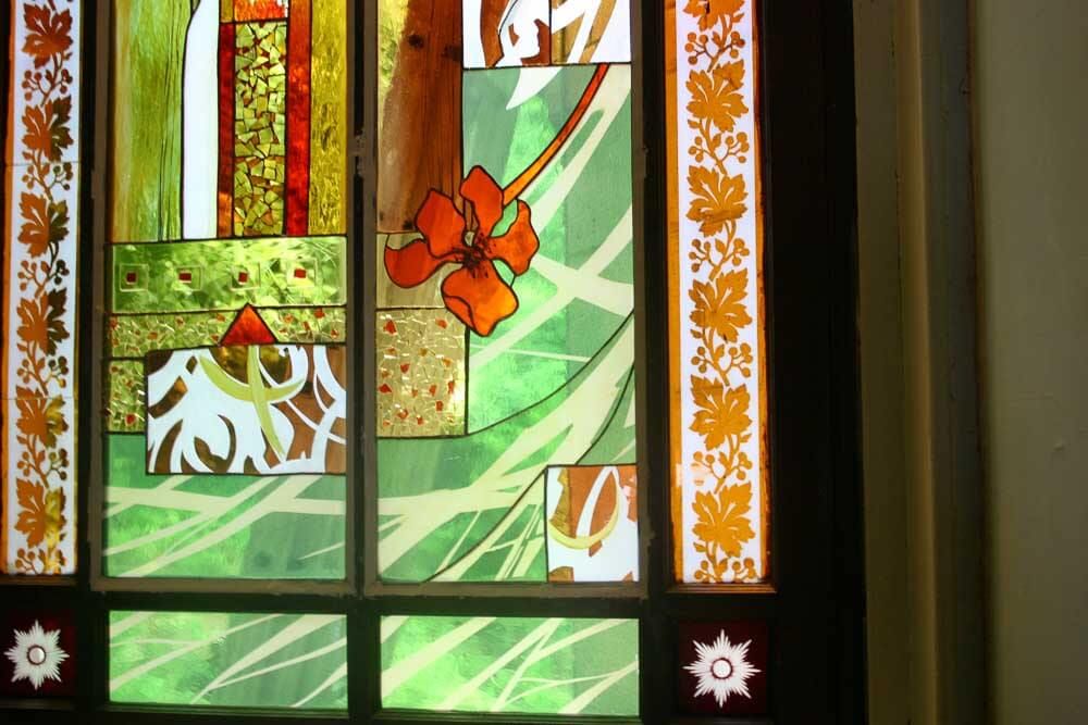 Vitrail orné de motifs floraux et de feuilles vertes, oranges et brunes.