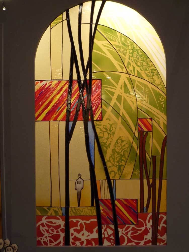 Vitrail : motif abstrait avec des motifs rouges, verts et jaunes, des lignes noires et une silhouette.