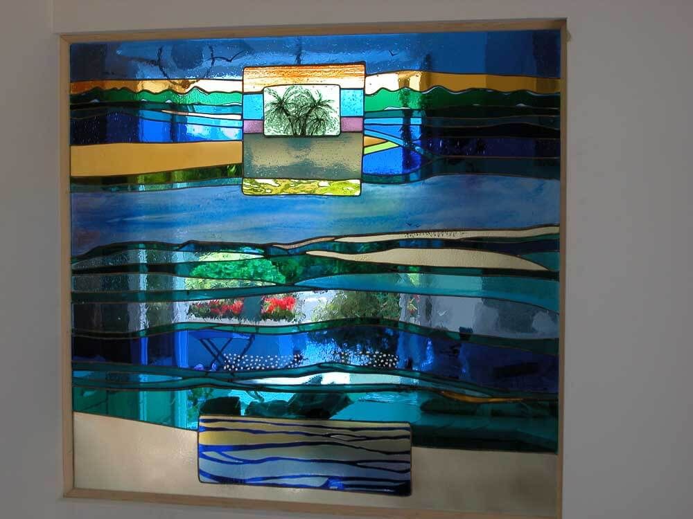 Vitrail représentant un paysage avec de l'eau, des arbres et un ciel dans des tons de bleu, de vert et d'or.