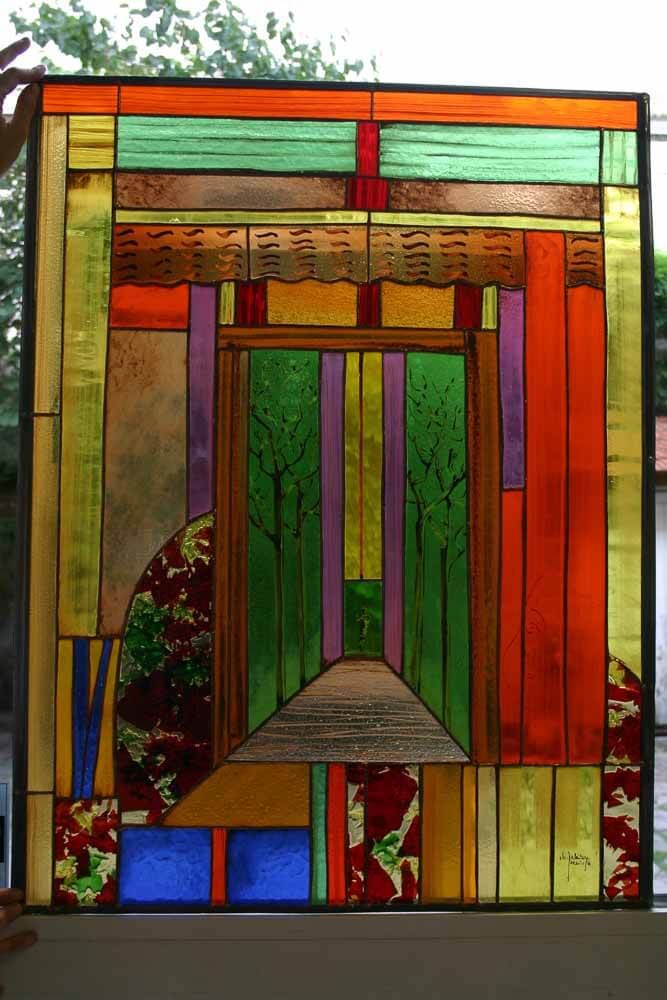 Vitrail à décor abstrait. Couleurs vertes, oranges, violettes et dorées. Représente des silhouettes d'arbres.