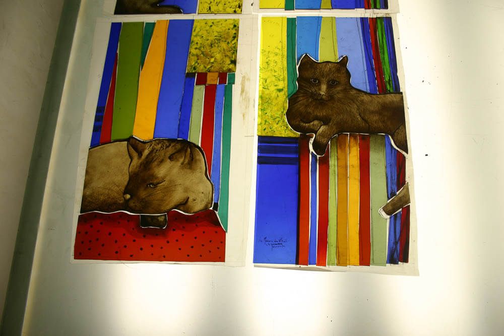 Vitrail représentant deux chats bruns sur un fond rayé coloré.