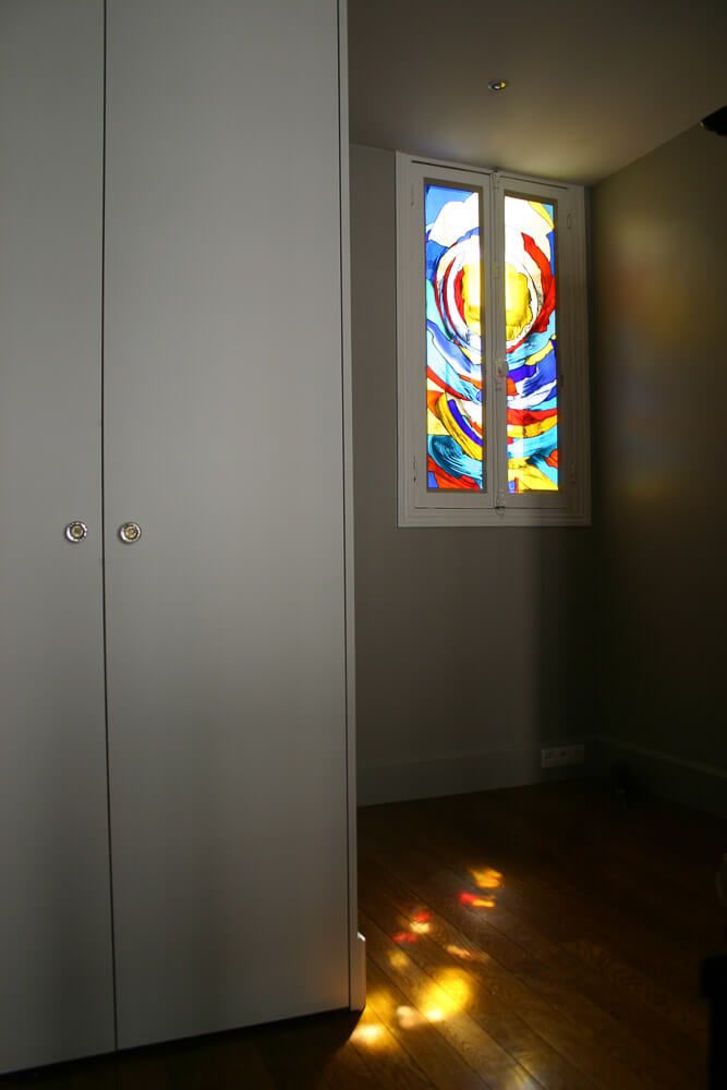 Placard blanc, vitrail projetant une lumière colorée sur le parquet.