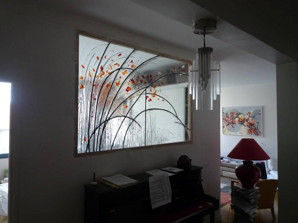 Panneau décoratif en vitrail à motif floral au-dessus d'un piano dans une pièce.