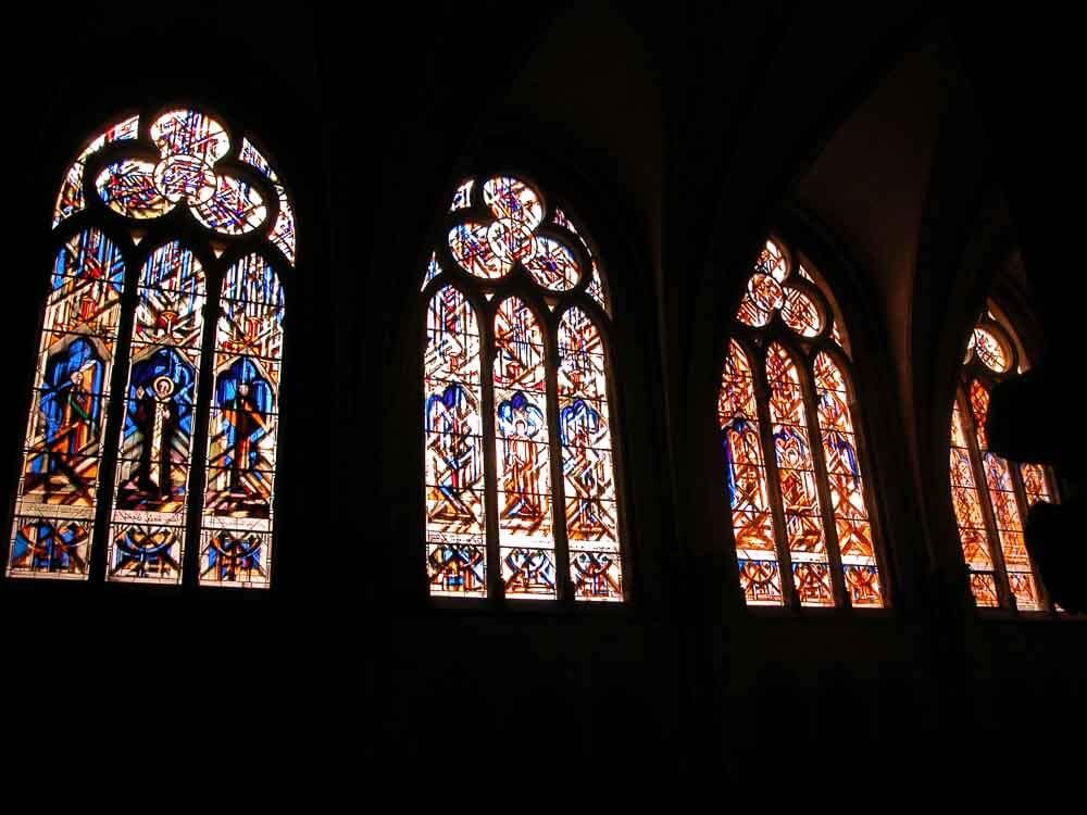 Des vitraux aux motifs détaillés et aux couleurs éclatantes, installés dans l'intérieur sombre d'une église.