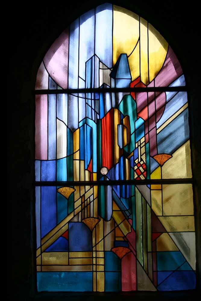 Vitrail représentant un paysage urbain abstrait aux formes géométriques colorées : bleu, rouge et jaune, avec un contraste entre les zones claires et foncées.