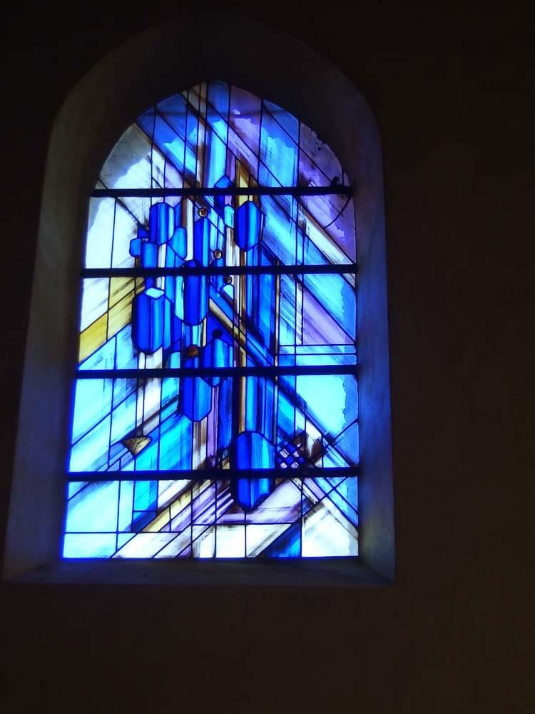 Vitrail orné de formes abstraites bleues et violettes dans un cadre arqué.