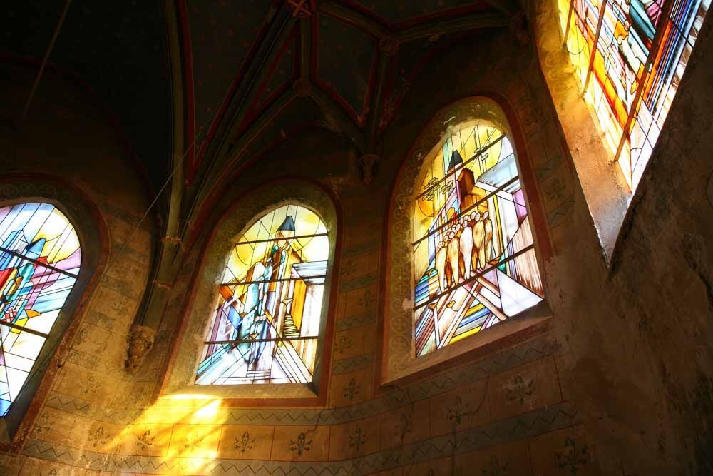 Vitraux d'une église en pierre, laissant entrer une lumière colorée. Arches ornées de personnages.