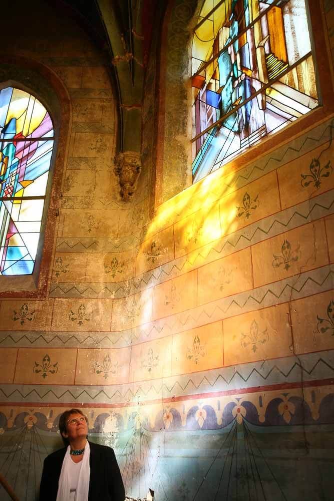 Un homme lève les yeux vers un vitrail ; la lumière du soleil le traverse et illumine le mur.