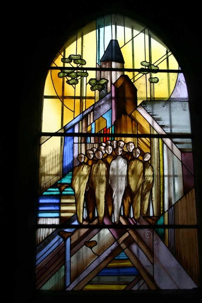 Vitrail représentant des personnages devant une église. Motif abstrait aux tons chauds.