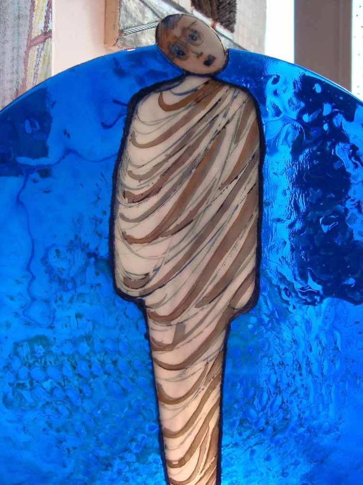 Vitrail d'une silhouette à rayures beiges et marron, sur fond bleu.