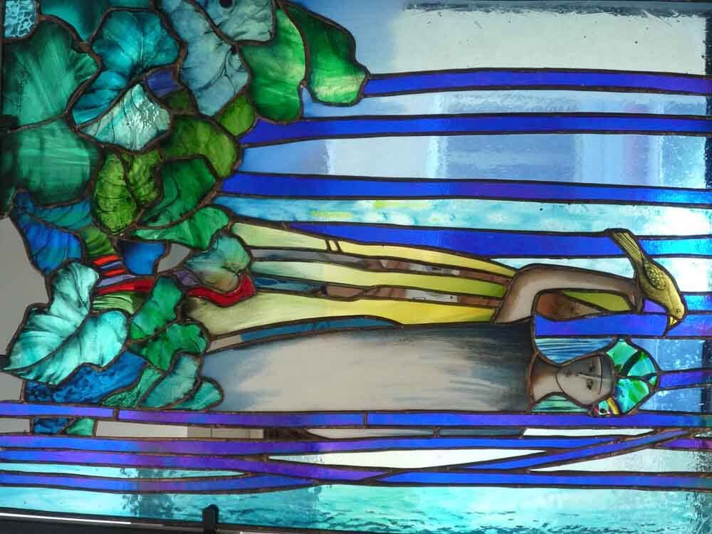 Vitrail représentant un personnage allongé sous un feuillage bleu et vert, avec un oiseau perché au-dessus.