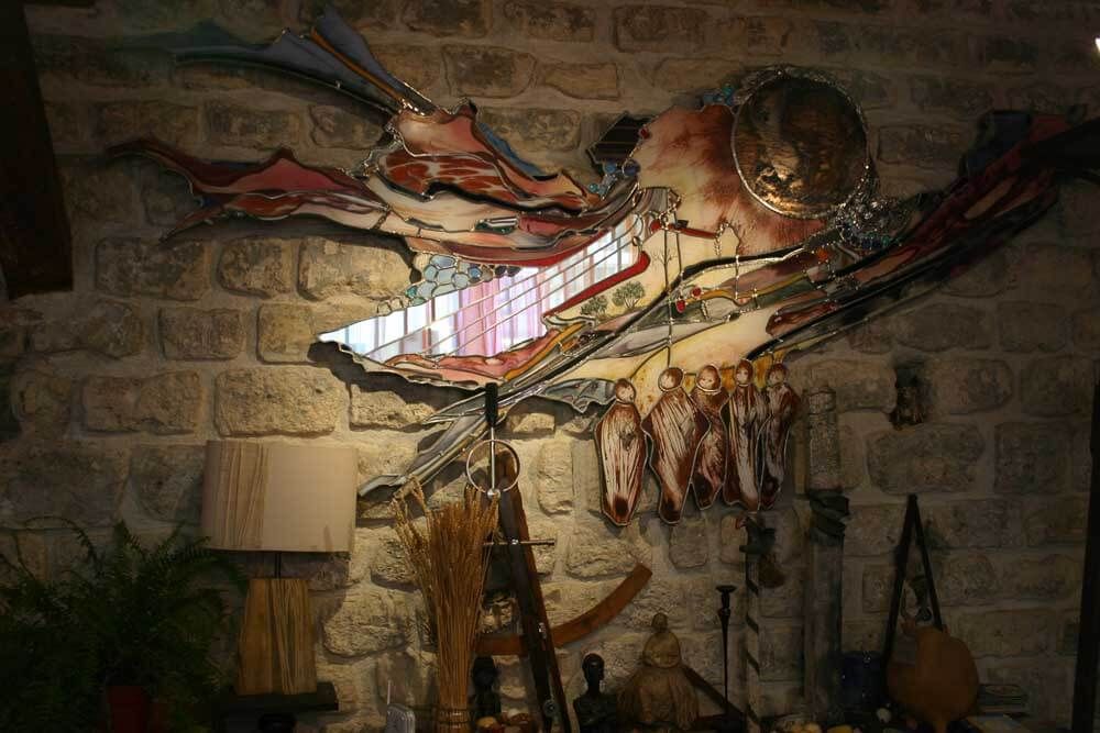 Vitrail représentant une créature stylisée ailée, fixé sur un mur de pierre, dans une pièce faiblement éclairée.