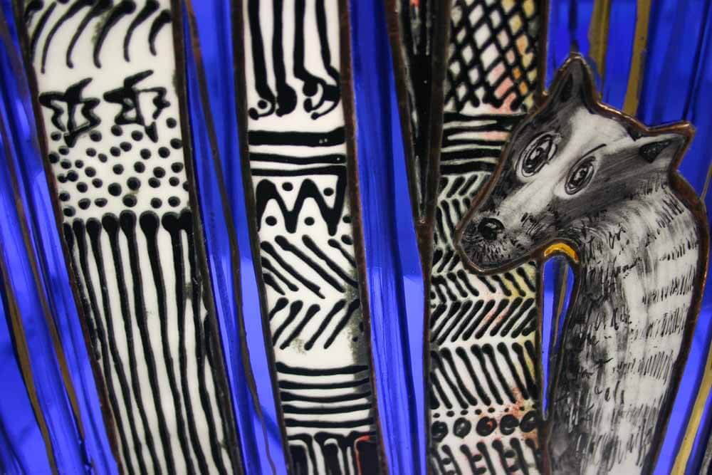 Gros plan sur un vitrail décoré de motifs noirs et blancs et d'une tête de loup gris. Fond bleu.