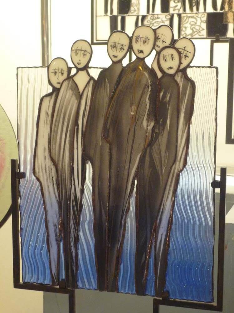 L'art du vitrail représente un groupe de personnages vêtus de vêtements sombres, sur un fond bleu aquatique.
