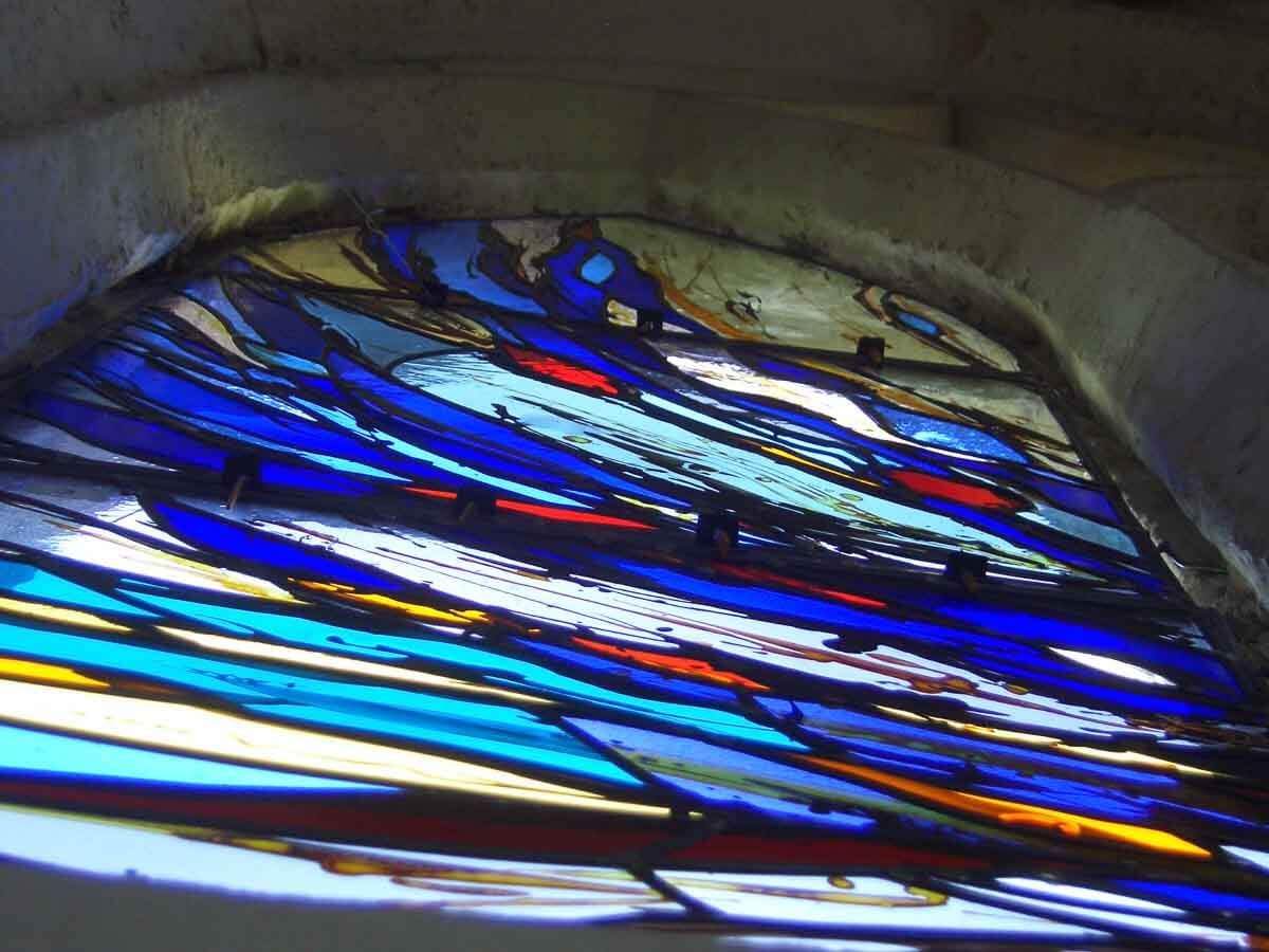 Vitrail à motif abstrait bleu, rouge et blanc, enchâssé dans une arche en pierre.