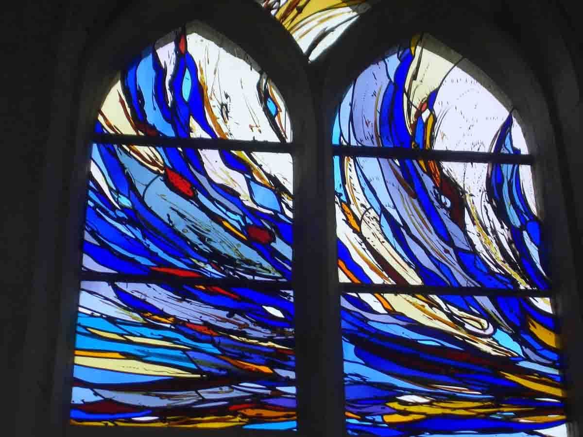 Vitrail à motif abstrait bleu et blanc, enchâssé dans une arche en pierre.