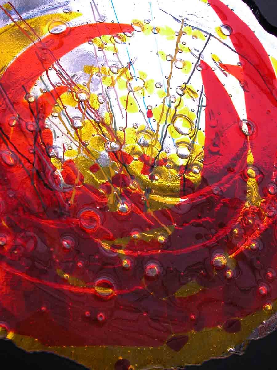 Vitrail abstrait composé de tourbillons de peinture rouge et jaune avec de petites bulles.