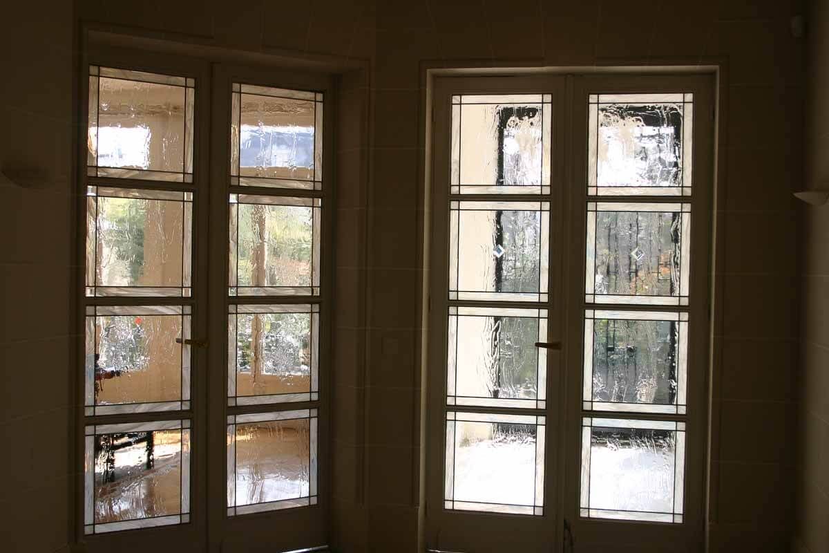 Deux portes vitrées à plusieurs panneaux et à cadre blanc. Vue extérieure à travers du verre dépoli ; murs brun clair.