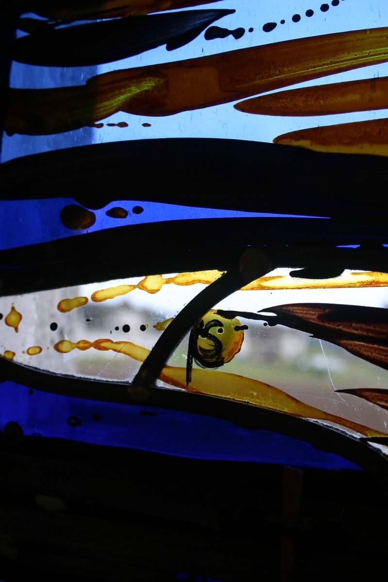 Vitrail orné de formes abstraites bleues, brunes et jaunes et d'un petit motif circulaire.