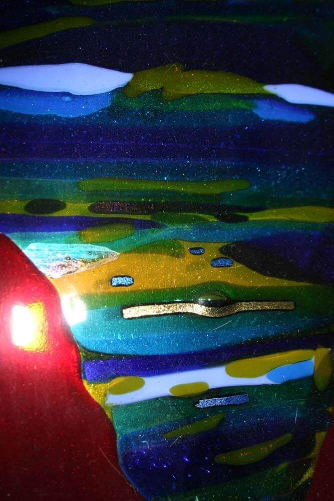 Œuvre abstraite en verre superposé. Des bleus, des verts, des jaunes et du blanc composent un paysage. Une lueur rouge apparaît à gauche.