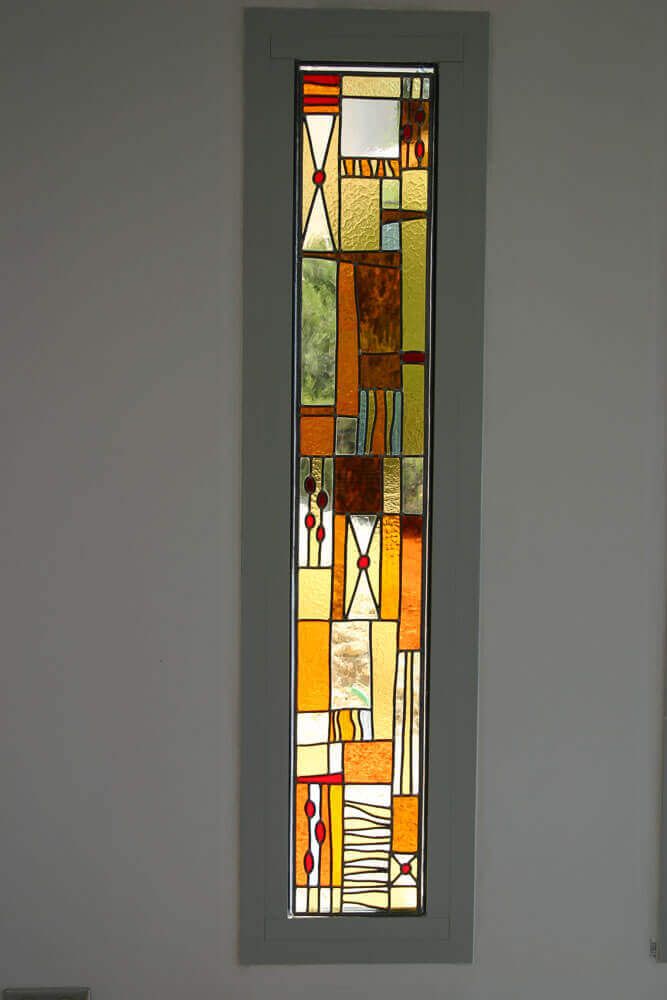 Vitrail rectangulaire étroit orné d'un motif abstrait de formes géométriques aux tons chauds.