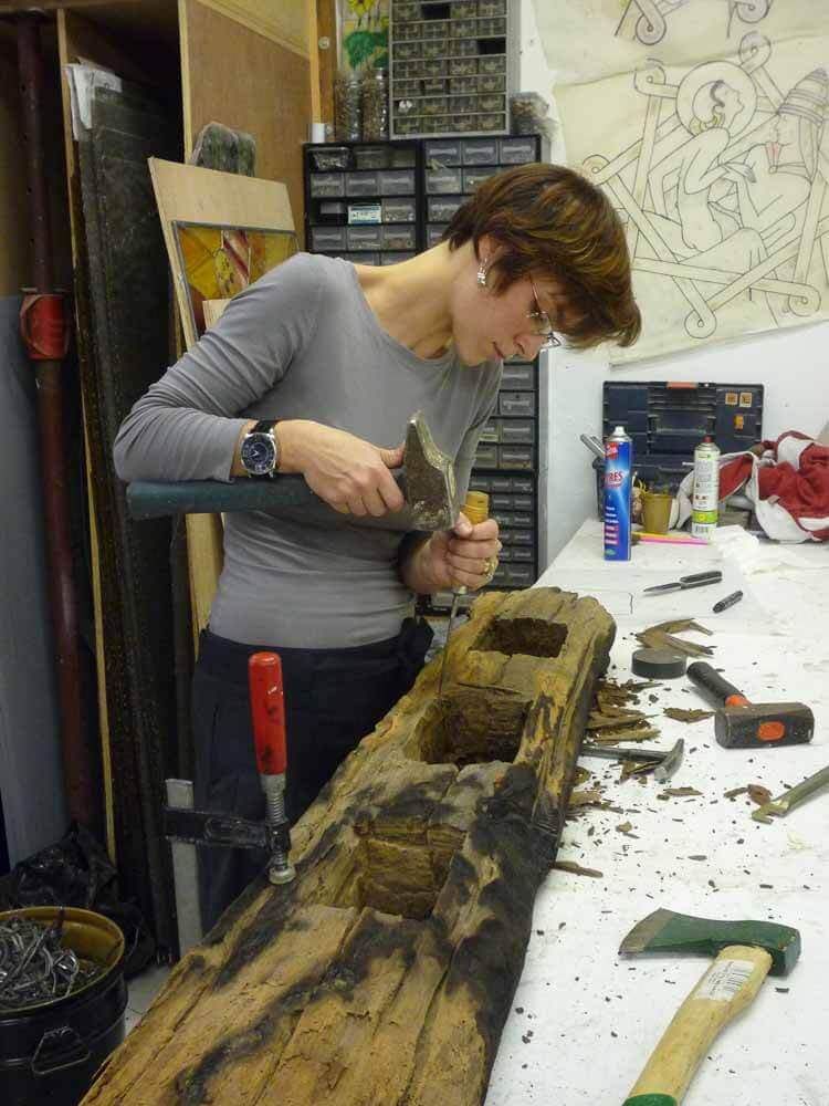 Une femme utilise un marteau et un burin pour sculpter du bois sur un établi dans un atelier.