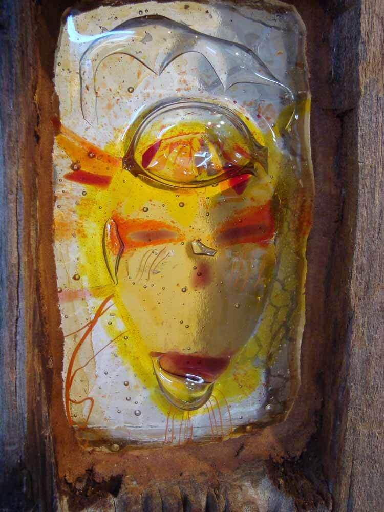 Visage en verre orné de détails orange et jaunes, serti dans du bois.