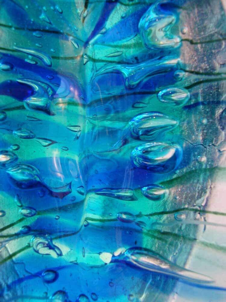 Gros plan sur une œuvre d'art en verre aux tons bleus et turquoise. Des gouttelettes d'eau adhèrent à la surface, reflétant la lumière.