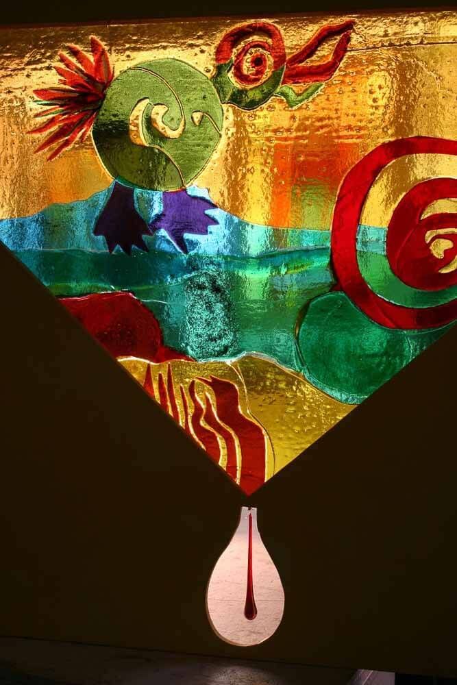 Vitrail représentant une créature verte fantaisiste avec des touches de rouge et d'orange, sur un fond abstrait et coloré.