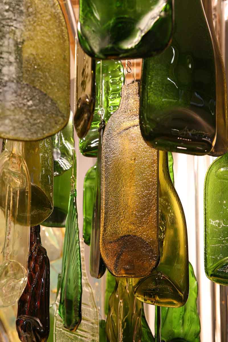 Vitraux en formes de bouteilles en verre recyclées vertes et jaunes se chevauchent, suspendues.