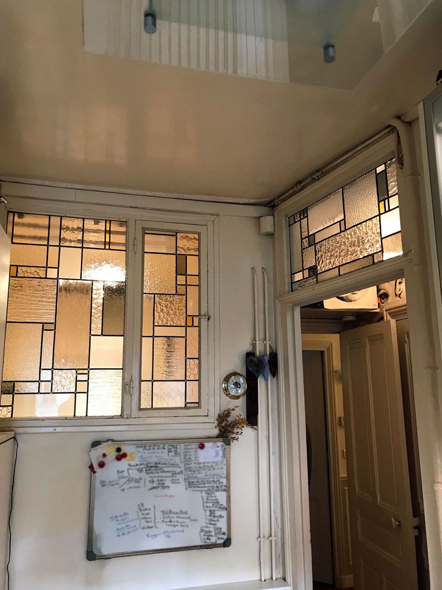 Couloir intérieur avec vitraux et tableau blanc au mur.