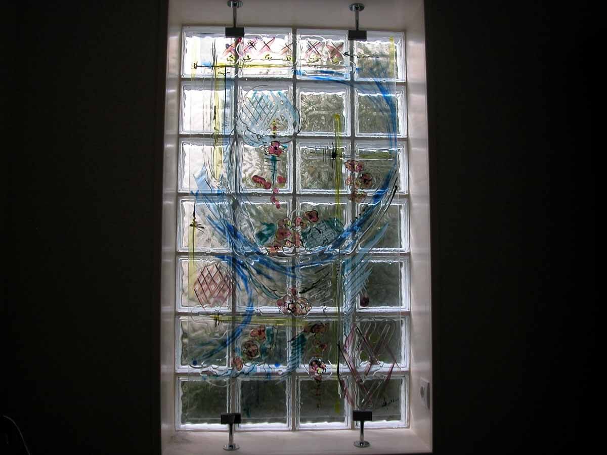 Fenêtre en pavés de verre avec éléments décoratifs bleus, rouges et jaunes.