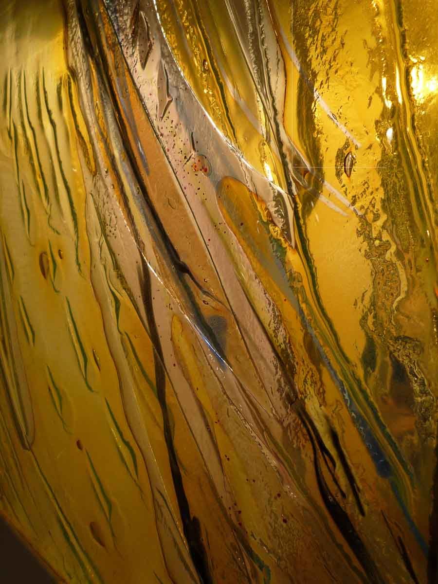 Gros plan abstrait d'un verre ambré strié de doré, de brun et de reflets bleutés, créant un motif fluide et réfléchissant.