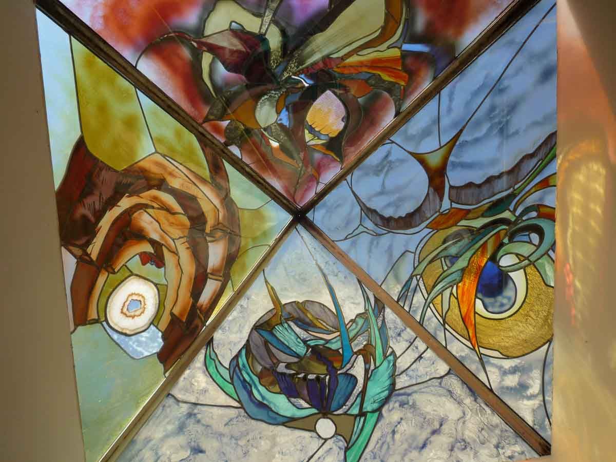 Plafond en vitrail orné de motifs floraux abstraits aux couleurs variées, encadré de bois brun.