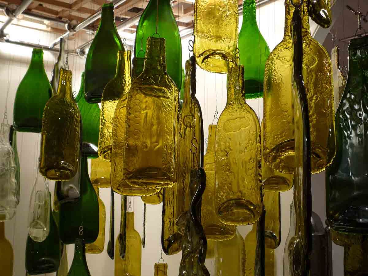 Vitraux en formes de bouteilles en verre vertes et jaunes sont suspendues au plafond.