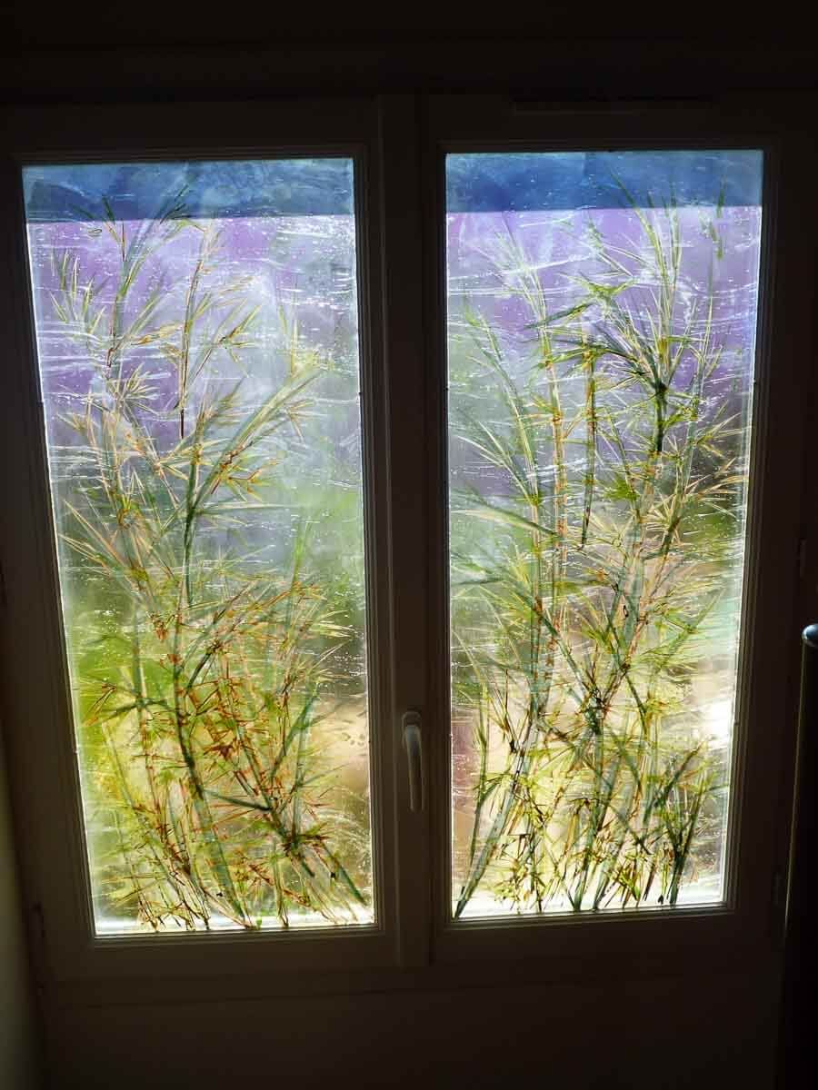 Fenêtre à deux vantaux ornée de tiges de bambou peintes. Les couleurs sont le vert, le jaune et le violet.