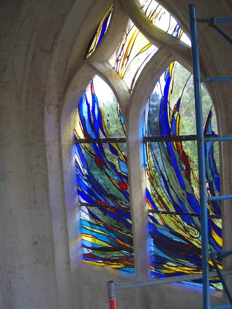 Vitrail orné de motifs abstraits bleus et jaunes. Une échelle d'échafaudage bleue se trouve à côté du vitrail.