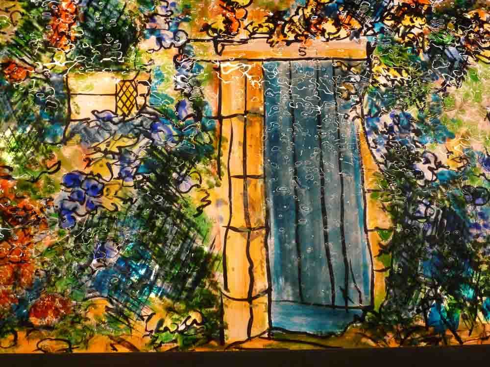 Une porte bleue entourée de fleurs et de feuillages colorés ; la lumière brille derrière.