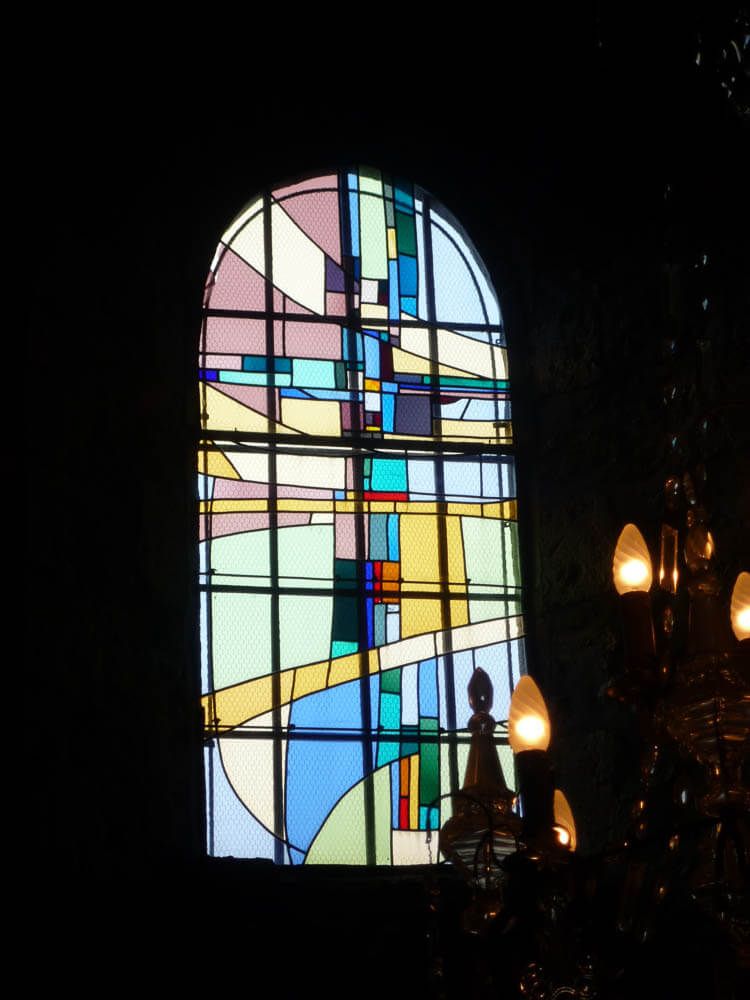 Vitrail à motif géométrique abstrait dans des tons de bleu, jaune et rose, à l'intérieur d'un bâtiment sombre.