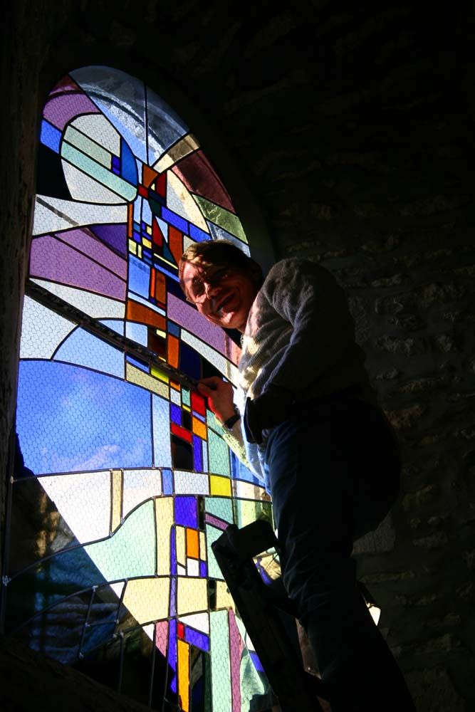 Une personne perchée sur une échelle travaille sur un vitrail coloré.